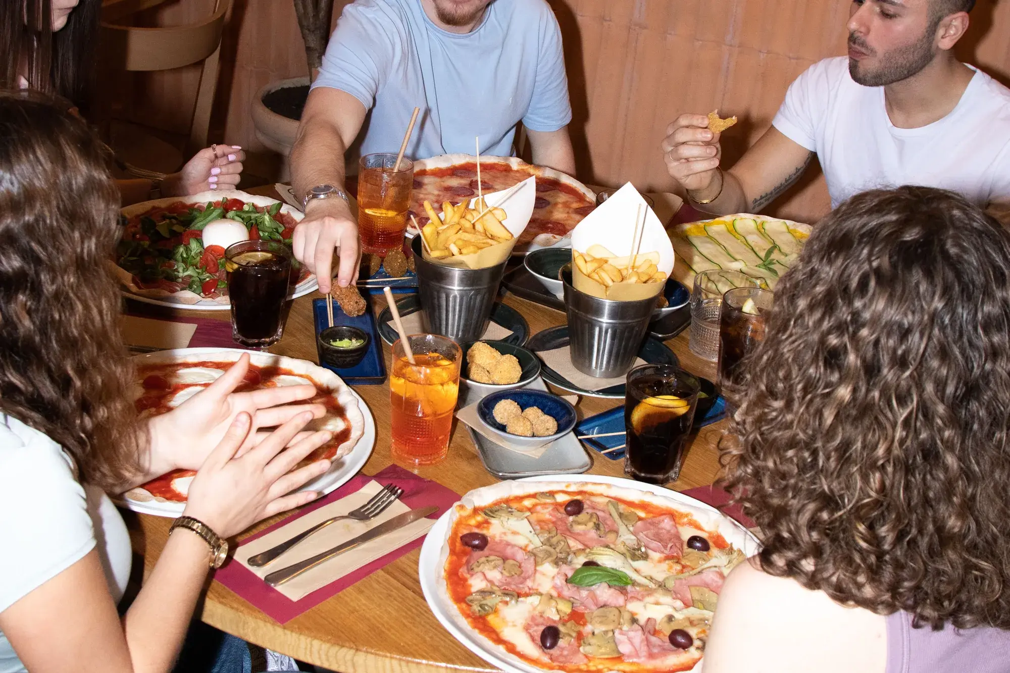 Una tavolata di ragazzi tra pizze, fritti e spritz