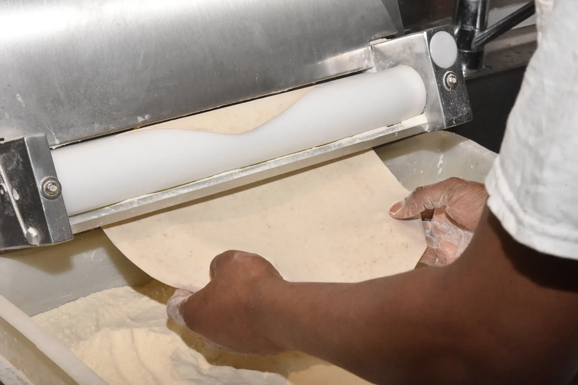 Hände führen Pizzateig durch die Teigausrollmaschine
