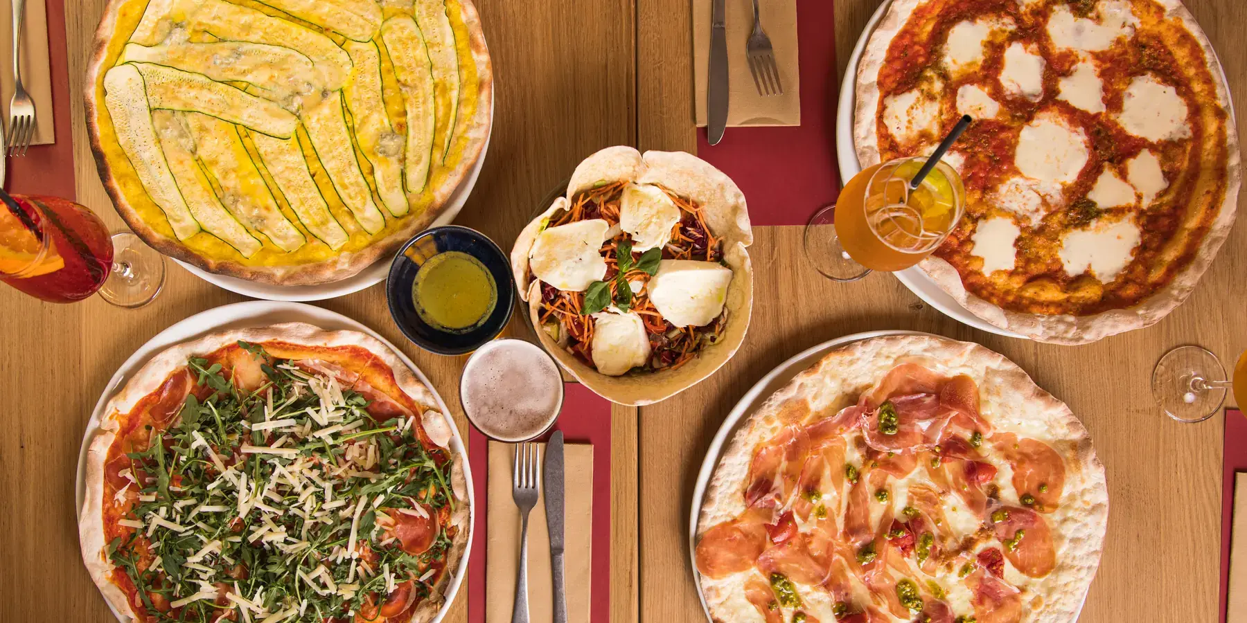Ein Tisch von oben: dünne Pizzen, ein Salat, Spritz und Pommes