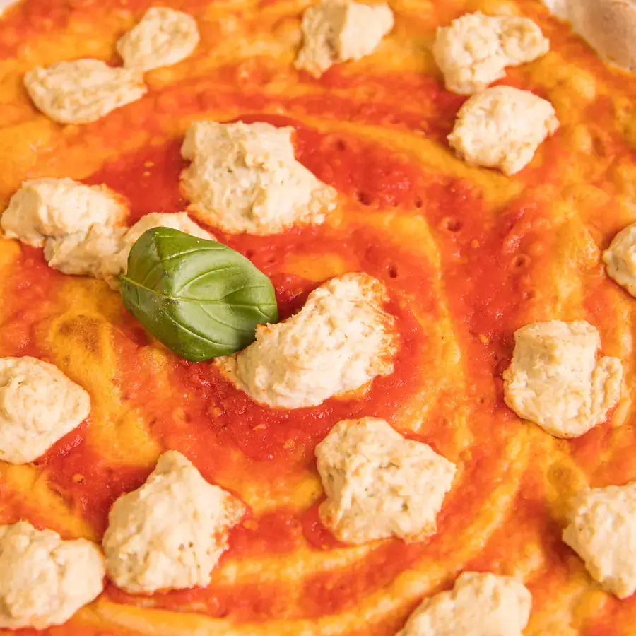 Pizza mit Tomatensauce, Flocken von pflanzlichem Käse und einem Basilikumblatt